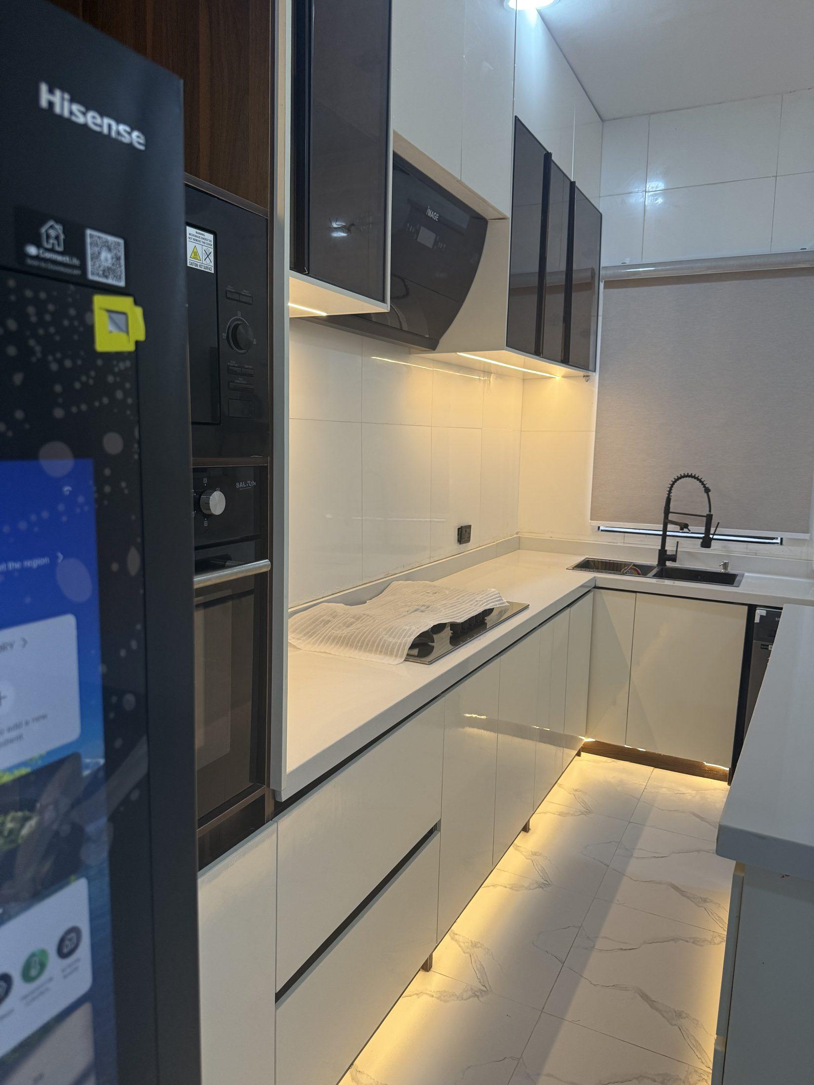 Run of cream gloss kitchen cabinets with under-cabinet and plinth lighting leading to a black sink and tap