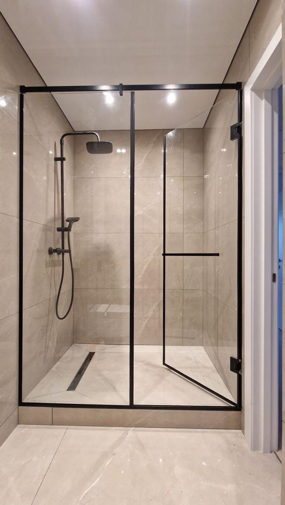 Walk-in shower with a black-framed glass screen and door, matt black rain shower and stone-effect tiles