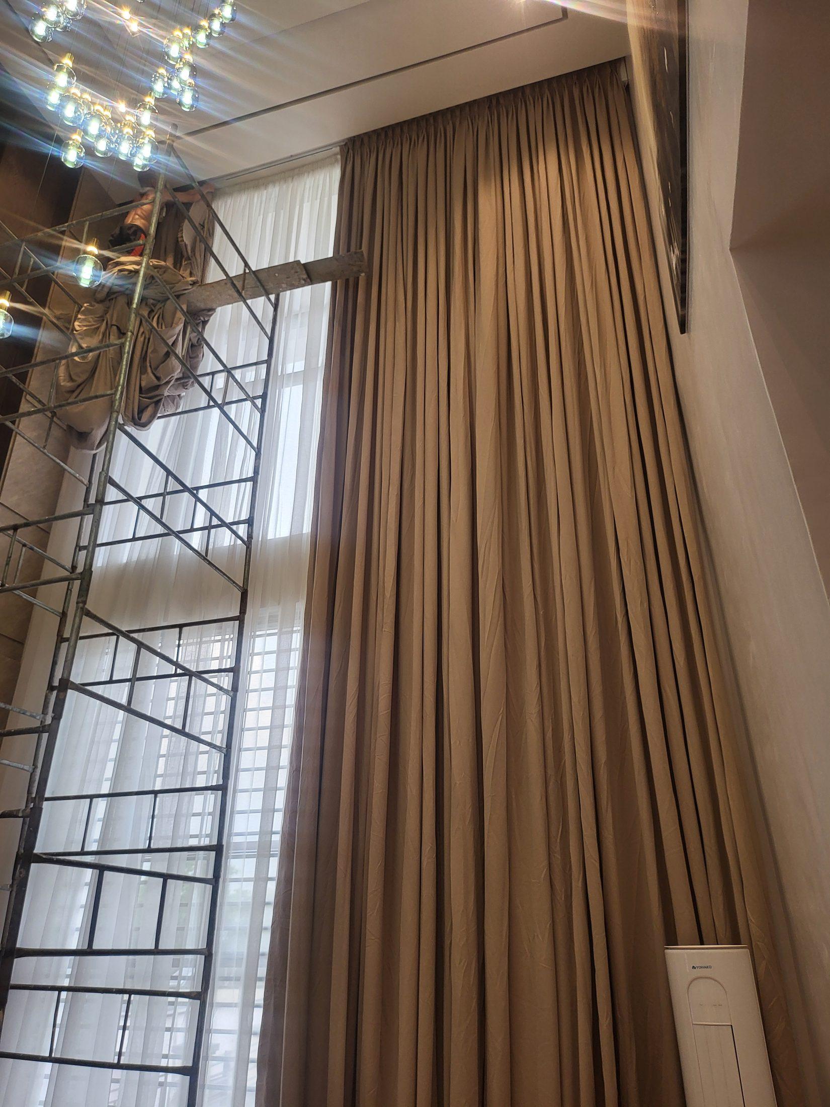Double-height pleated curtains and sheers being hung from scaffolding beside a glass chandelier