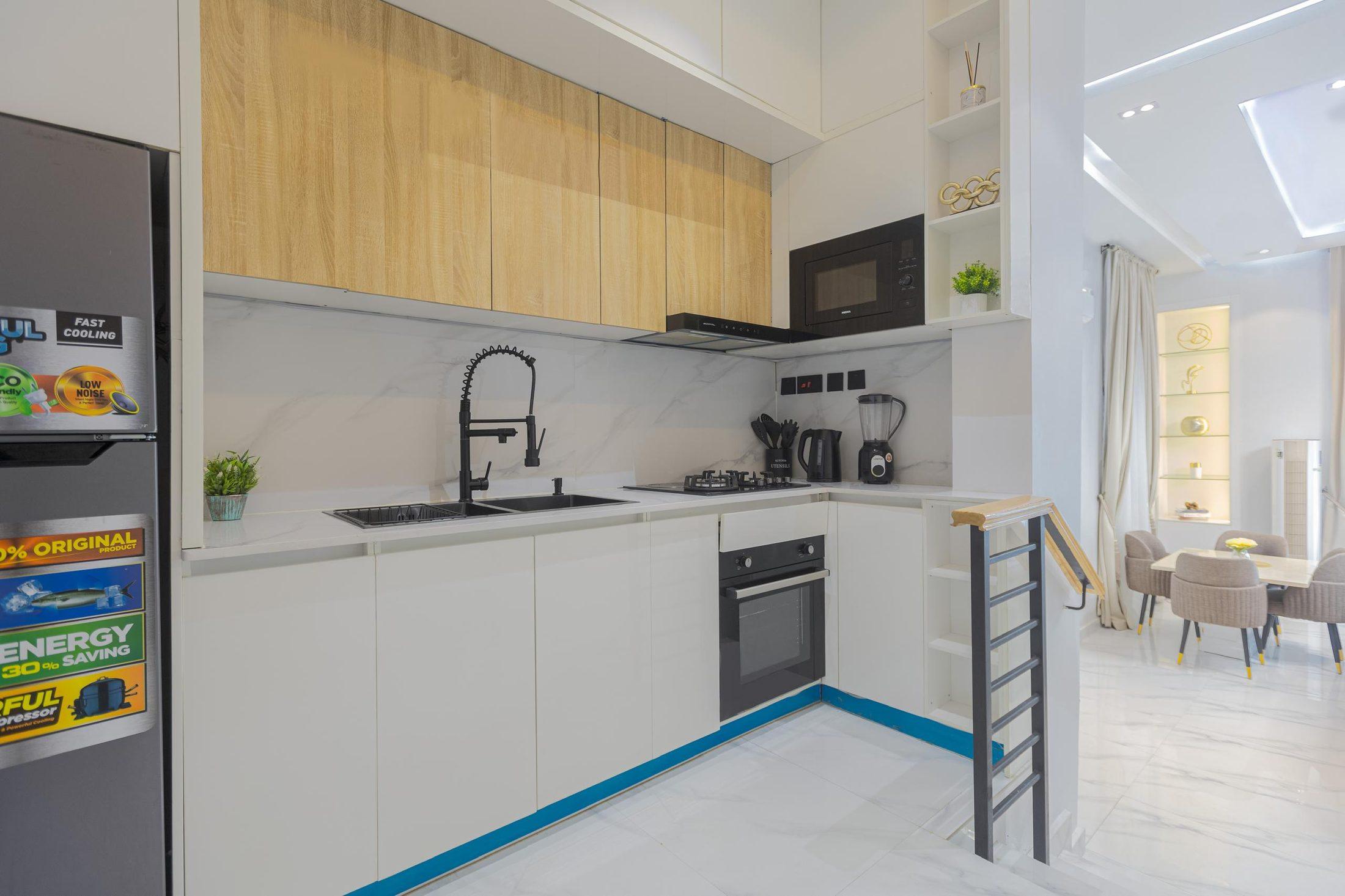 White and oak kitchen opening onto a bright dining area, with black metal stair railing
