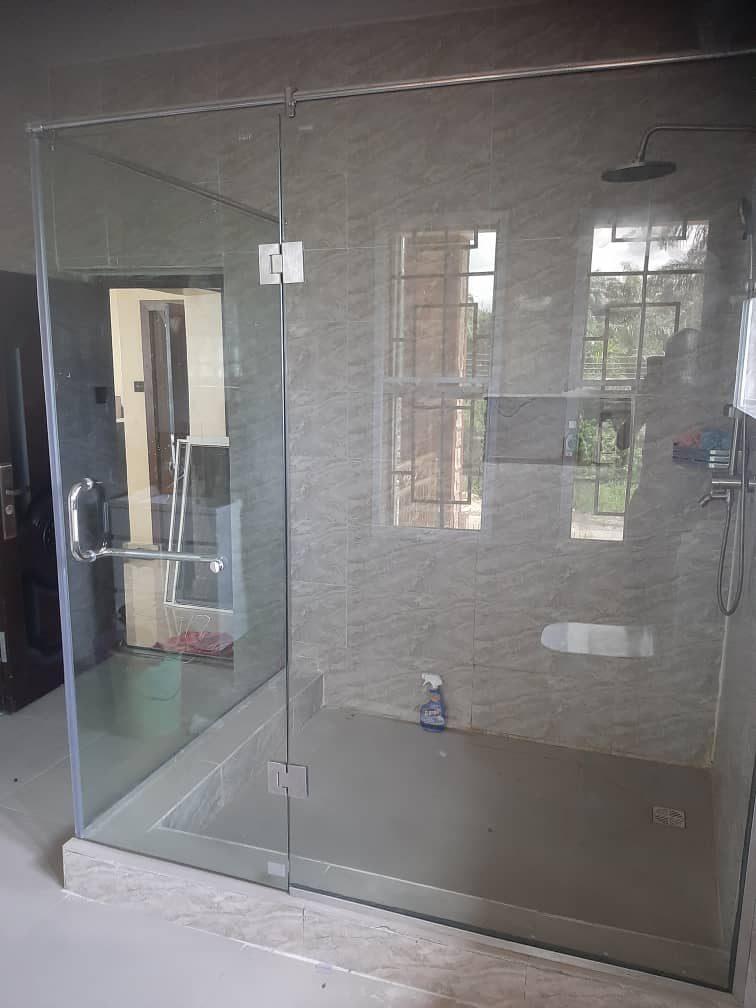 Frameless glass shower enclosure with polished hinges and handle on a tiled shower tray