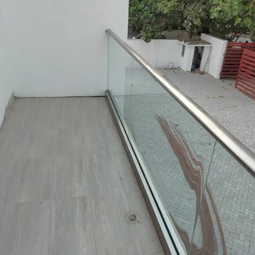 Frameless glass balcony balustrade with a brushed steel handrail above a paved courtyard