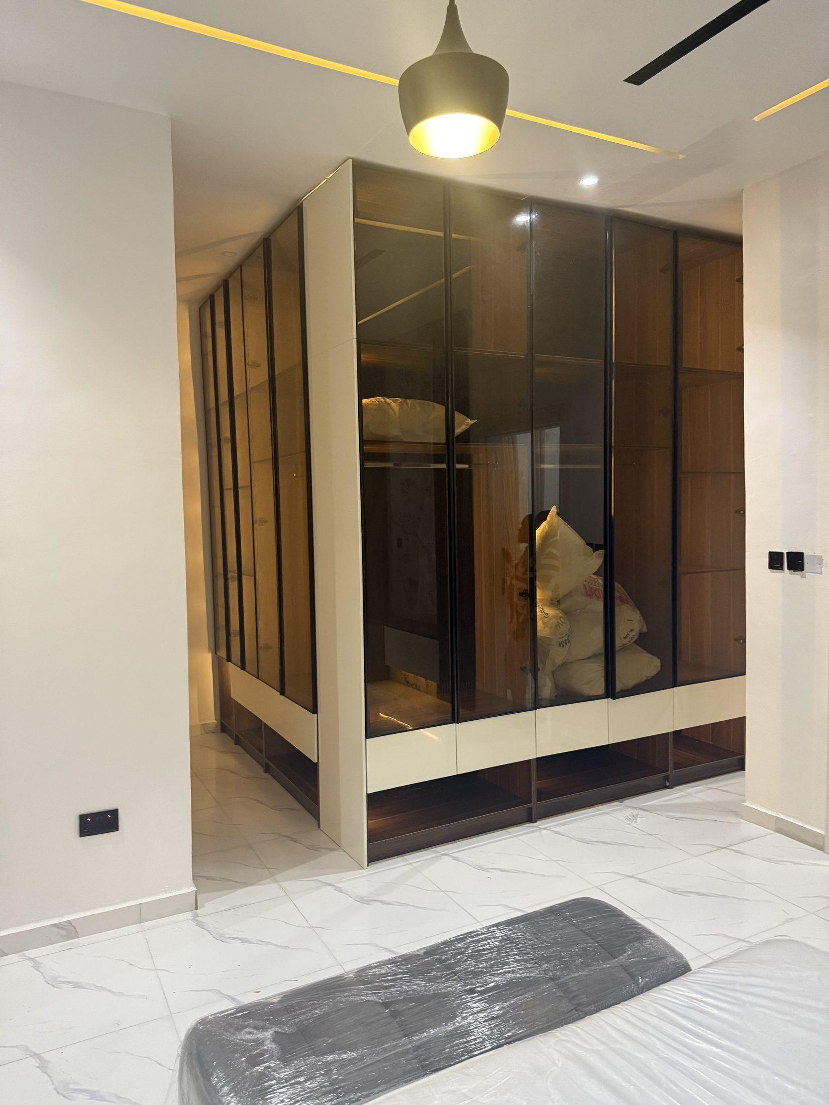 Corner walk-in wardrobe with black-framed smoked glass doors, timber interiors and cream gloss bases with open shoe shelves