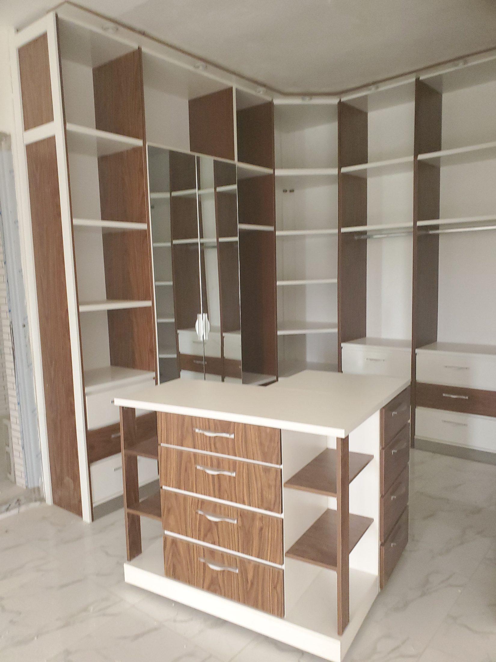 Walk-in wardrobe in walnut and white with open shelving, mirrored doors, hanging rails and a central island of walnut drawers
