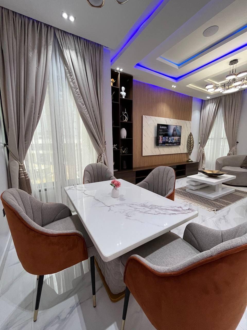 Marble dining table with grey and rust upholstered chairs, opening onto a lounge with a fitted media wall