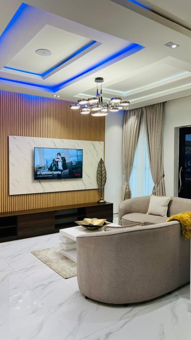 Living room with a timber-slatted media wall, curved boucle sofa, layered ceiling and chandelier